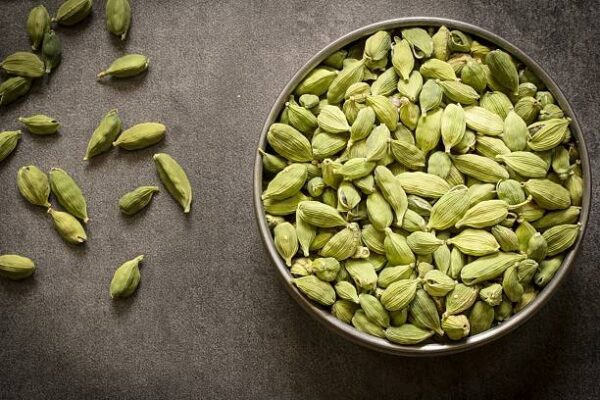 green cardamom pods in steel bowl with wooden background top view flat lay Cardamom